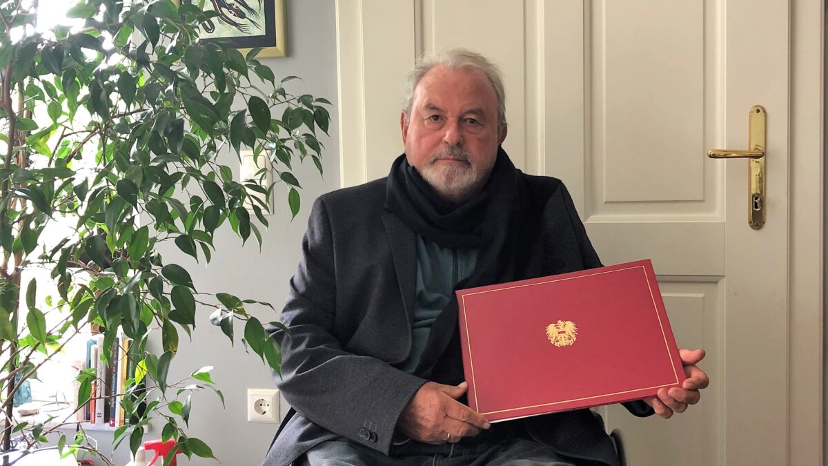 Dr. Voget hält eine schmuckvolle Mappe mit österreichischem Wappen darauf