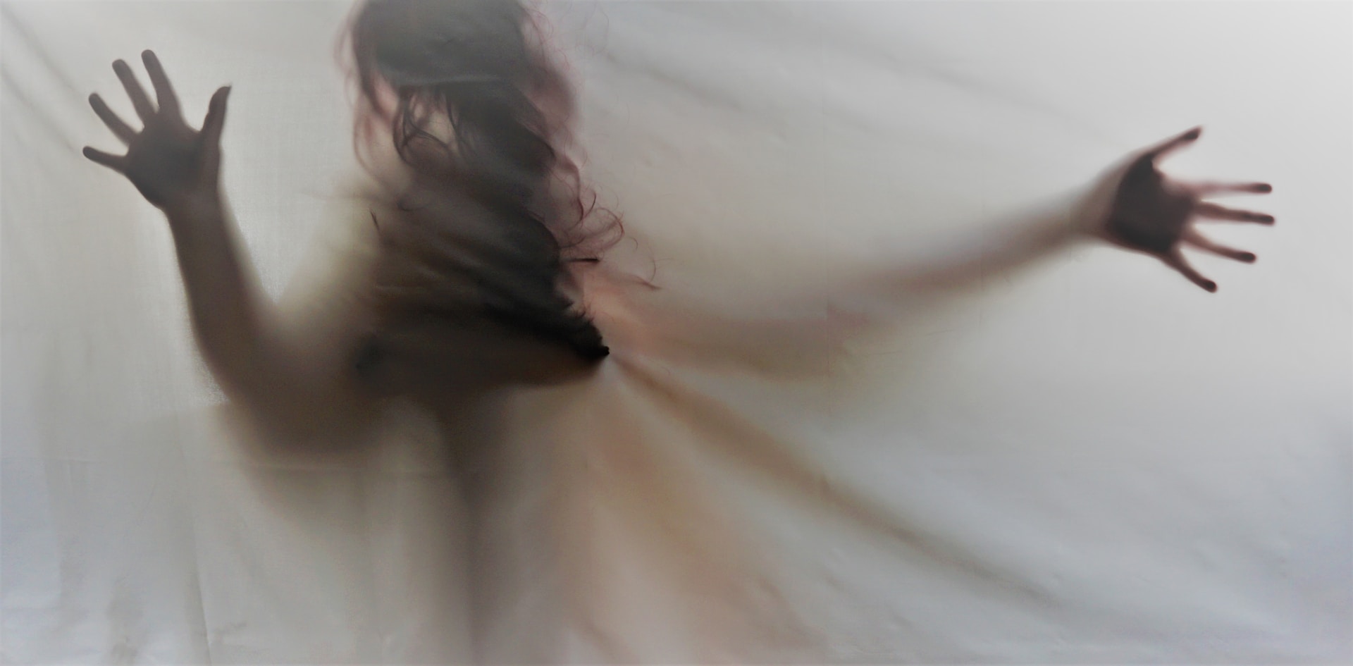 Schatten einer Frau mit langem Haar und Kleid hinter einer Leinwand