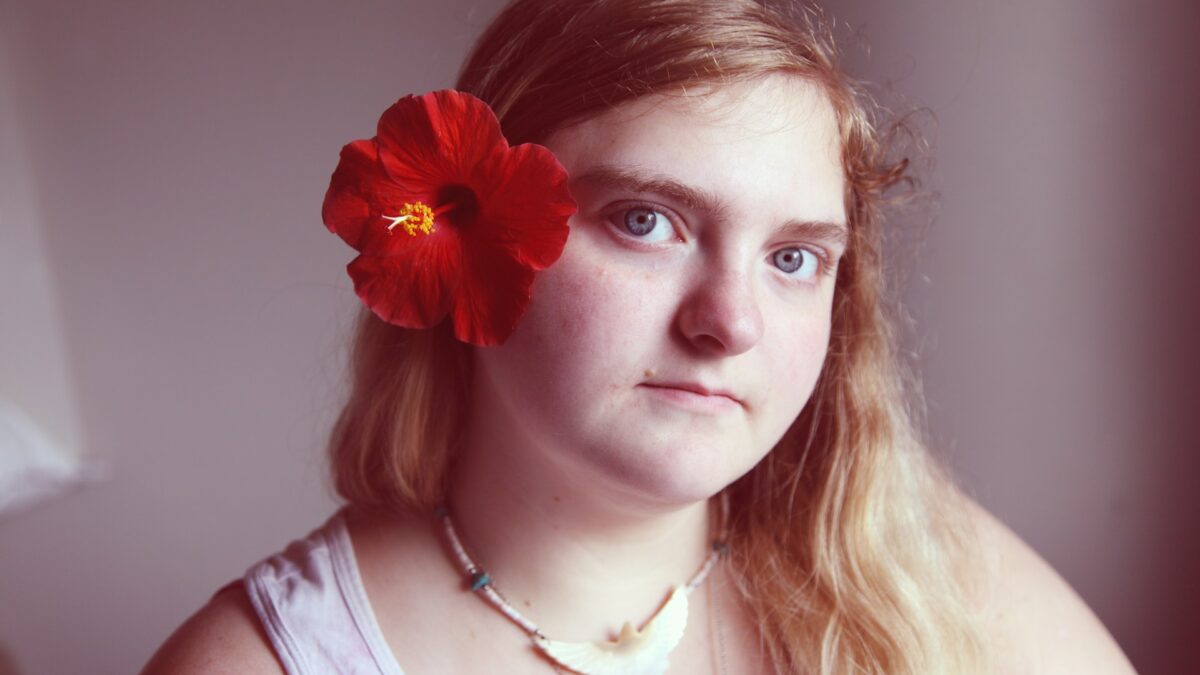 junge Frau mit roter Blume im langen Haar blickt in die Kalmera