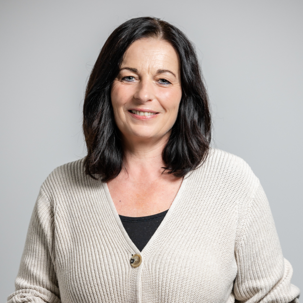 Portraitfoto von Silvia Kunz, sie hat langes, dunkles Haar und trägt eine schwarze Bluse und eine beige Weste