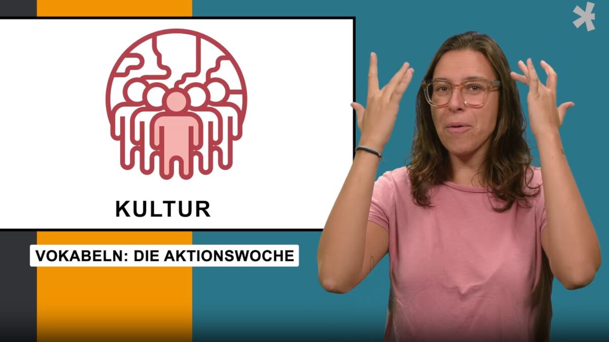 Screenshot Gebärdenwelt.t:v. Frau mit braunen Haaren und Brille gebärdet Vokabeln aus dem Bereich Kultur. "Kultur. Vokabeln: Die Aktionswoche"