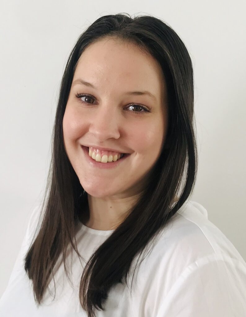 Portraitfoto Mag.a Victoria Biber, LL.M., sie hat braunes, langes Haar, trägt ein weißes Shirt ud lächelt in die Kamera