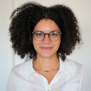 Portraitfoto Mag.a Nicola Onome Sommer (vormals Asiemo), sie hat offen getragene, schwarze, krause Haare, trägt eine Brille und eine weiße Bluse