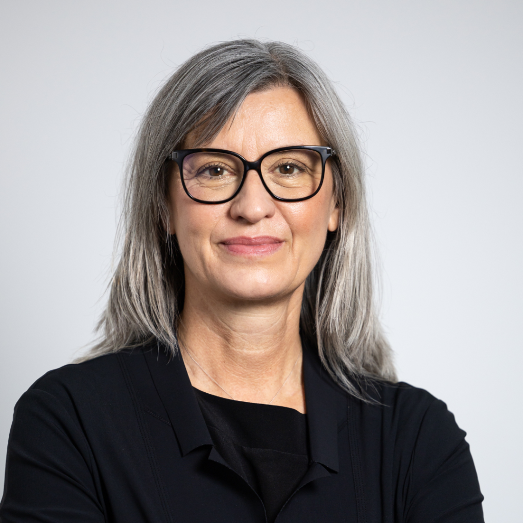 Portraitfoto von Anki Egger, sie hat graues, langes Haar, trägt eine schwarze Brille und einen schwarzen Pulli