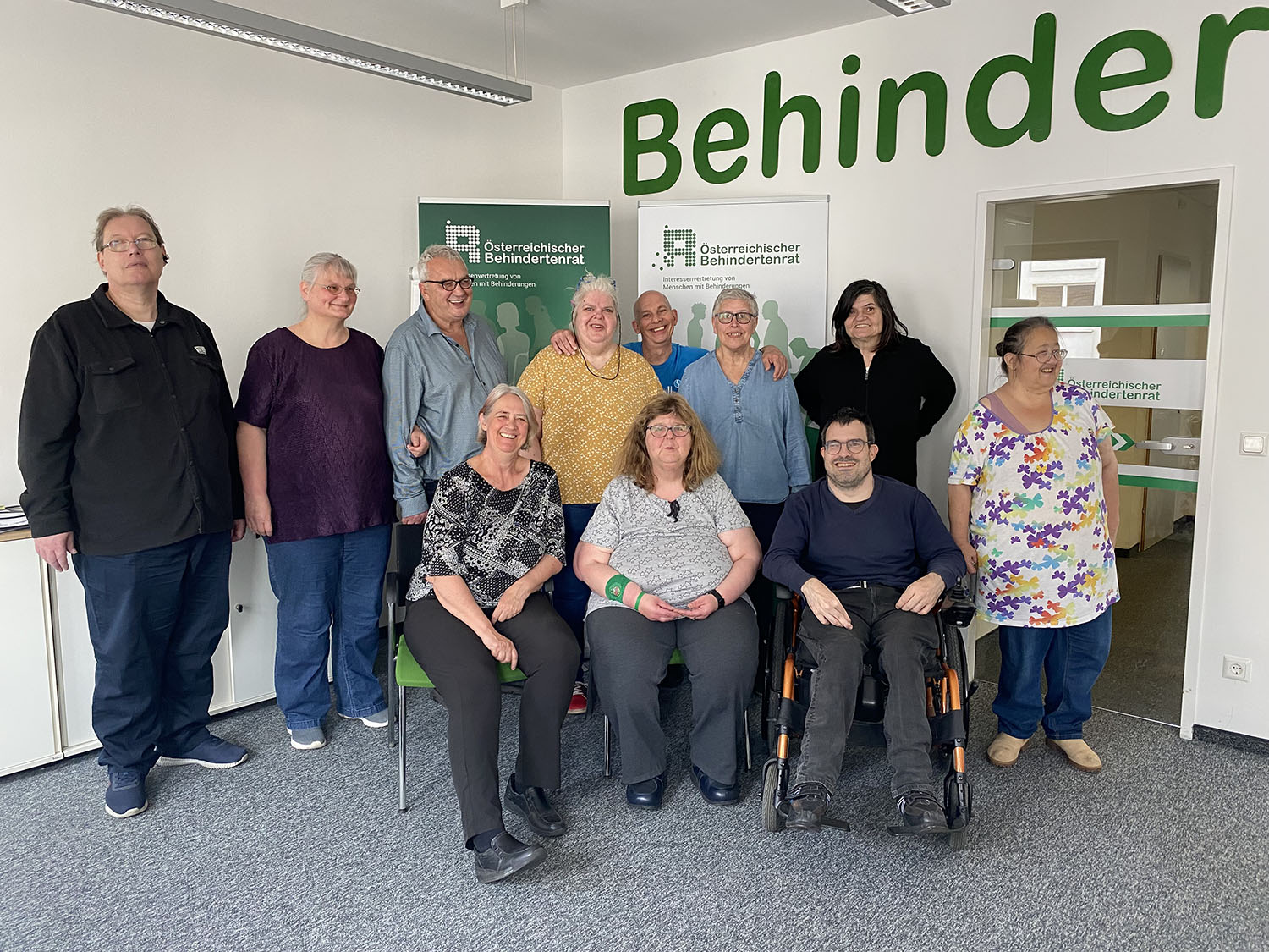 Gruppenbild von 8 stehenden und drei sitzenden Personen vor dem Rollup des Österreichischen Behindertenrats