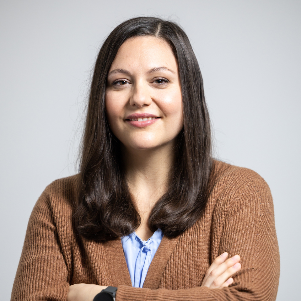 Portraitfoto von Gudrun Eigelsreiter, sie hat lnages, braunes Haar, verschränkte Arme, trägt eine blaue Bluse und darüber einen braunen Pulli