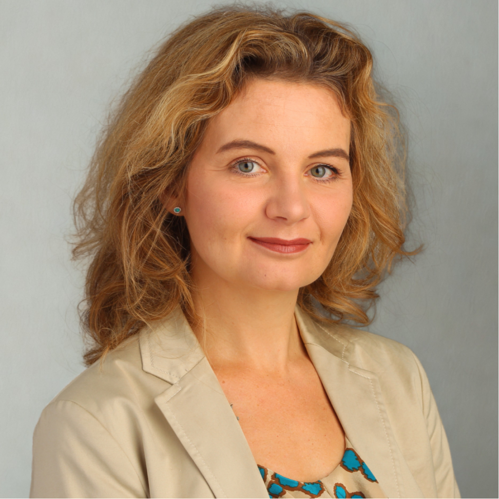 Portrait Kerstin Huber-Eibl, sie hat dunkelblondes, langes Haar, trägt ein Kleid und darüber ein beiges Sakko