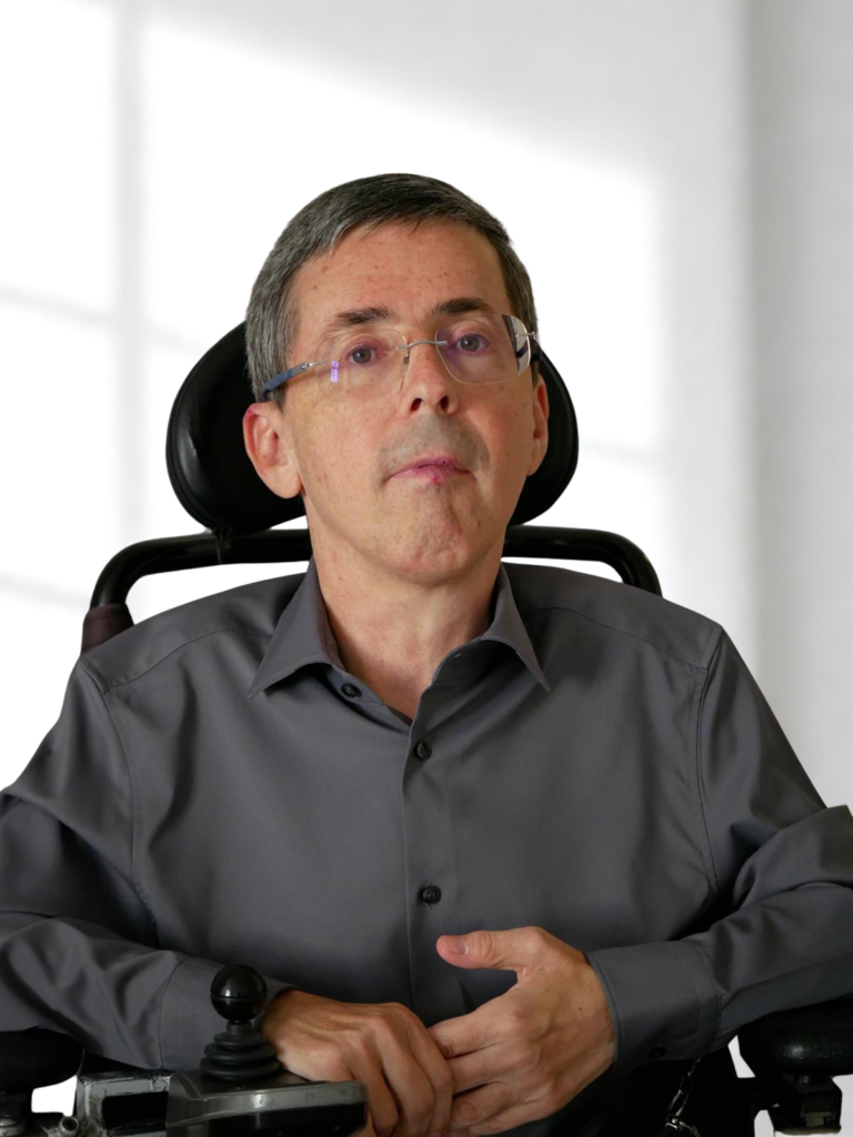 Portrait Martin Ladstätter, MA, er trägt eine gestelllose Brille und ein graues Hemd, sitzt in einem Rollstuhl
