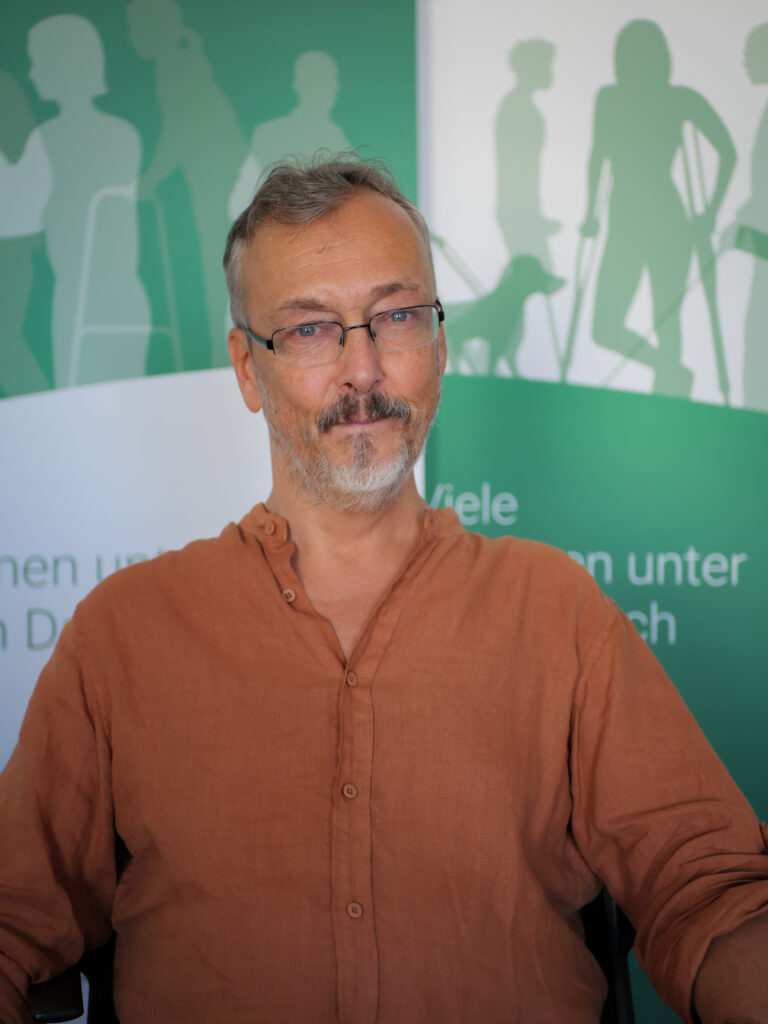 Klaus Widl, Mann mit grauem Haar und Brille, trägt ein braunes Hemd und blickt in die Kamera