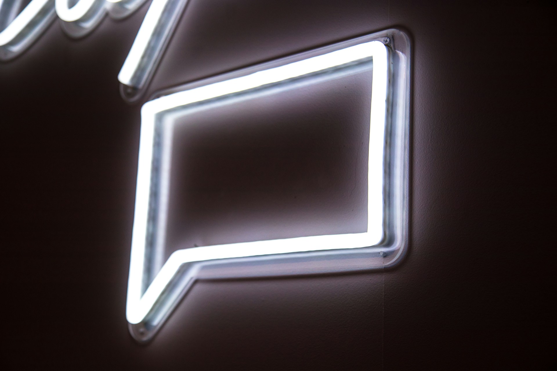 schwarzes Rechteck mit Leuchtzeichen in weiß, das eine Sprechblase darstellt, Foto: Unsplash/Jason Leung