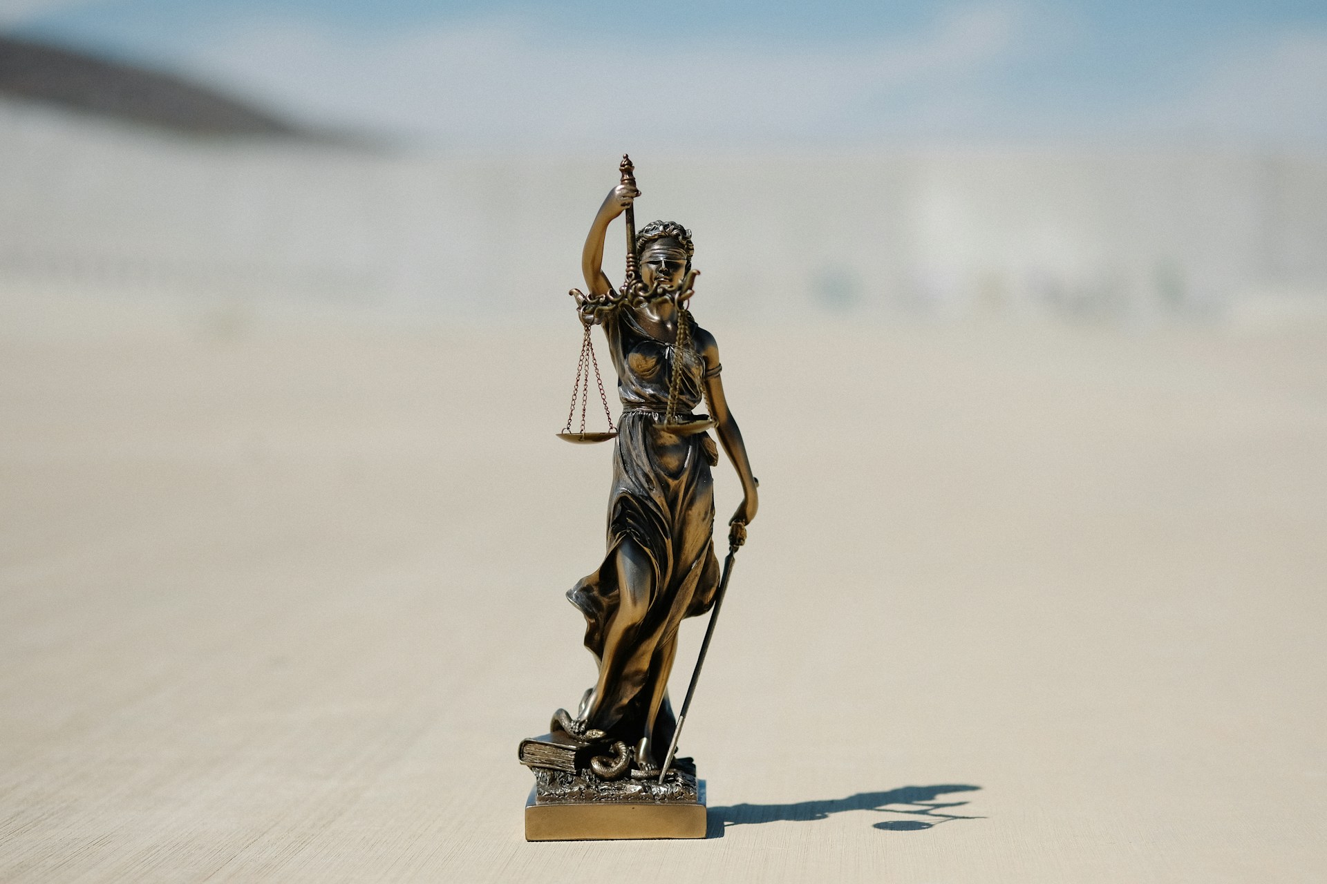 Statue der Justizia mit Waage in Bronze, die Statue steht auf hellem Untergrund. Foto: Unsplash/Wesley Tingey