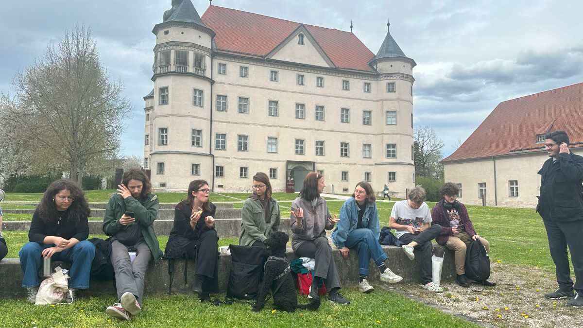 mehrere Menschen sitzen auf dem Grasboden vor dem Schloss Hartheim