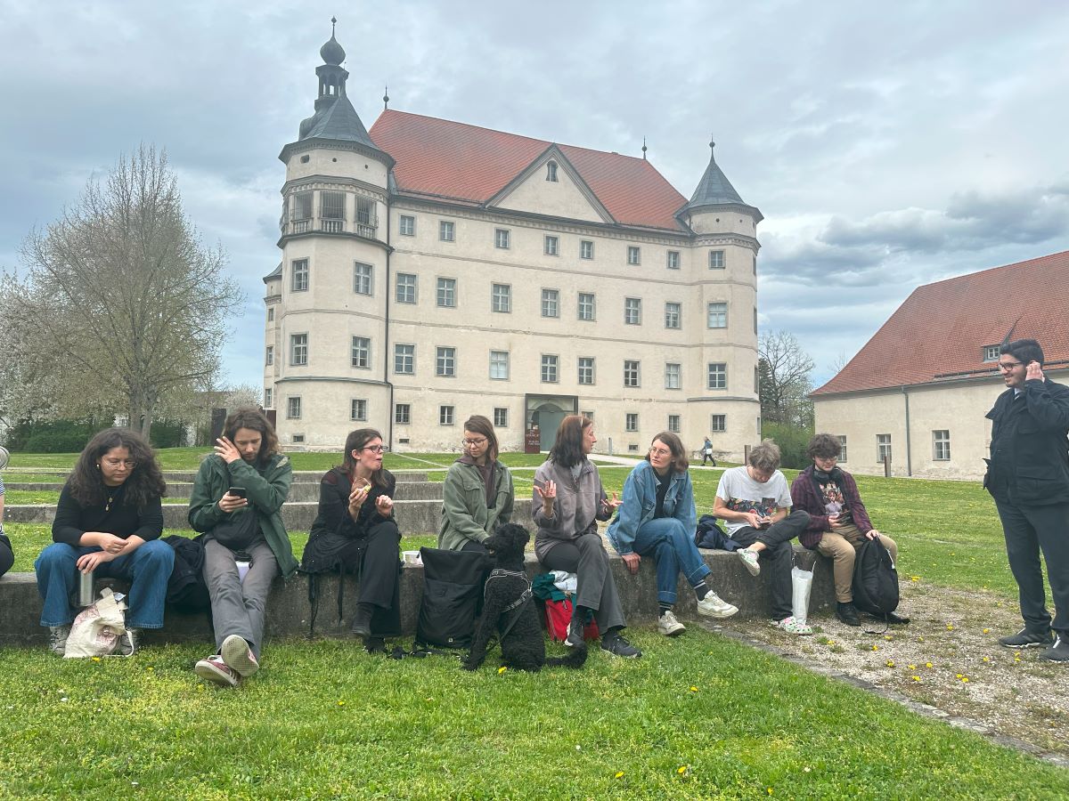 mehrere Menschen sitzen auf dem Grasboden vor dem Schloss Hartheim