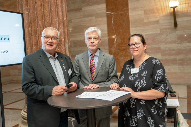 3 an einem Tisch sstehende Personen in der Säulenhalle des Parlaments