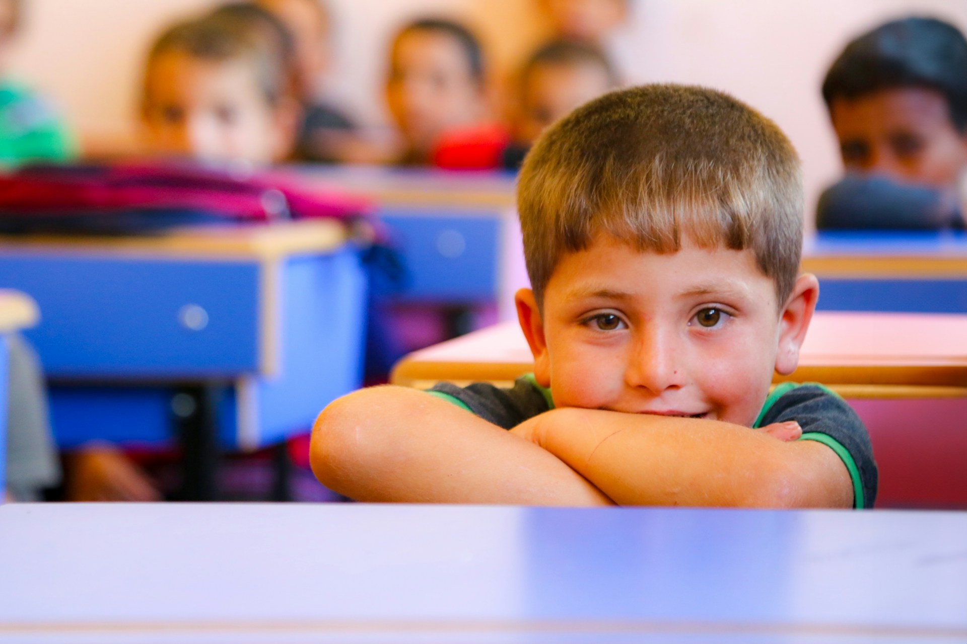 Schulklasse: Kinder sitzen vor ihren Tischen, im Vodergeund ein auf seine Unterarme gestützter Junge, Foto: Unsplash/‪Salah Darwish