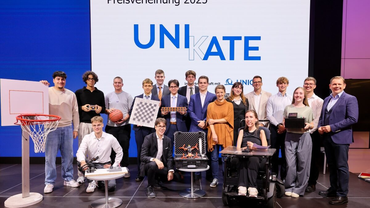Gruppenfoto von 18 Personen, die auf einer Bühne vor einem Screen mit dem Logo "UNIKATE" stehen. Zwei dieser Personen knien, eine sitzt im Rollstuhl. Alle Schüler präsentieren ihre Unikate