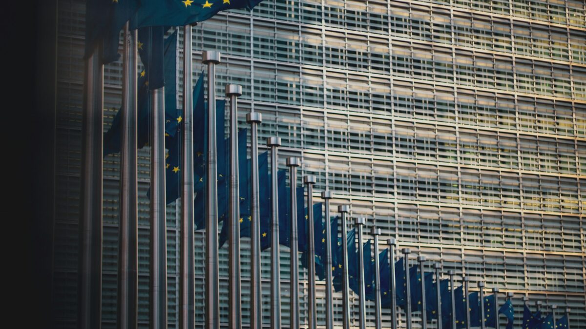 Gebäude mit riesigen Glasfenstern, davor wehen EU-Flaggen, Foto: Unsplash/Christian Lue