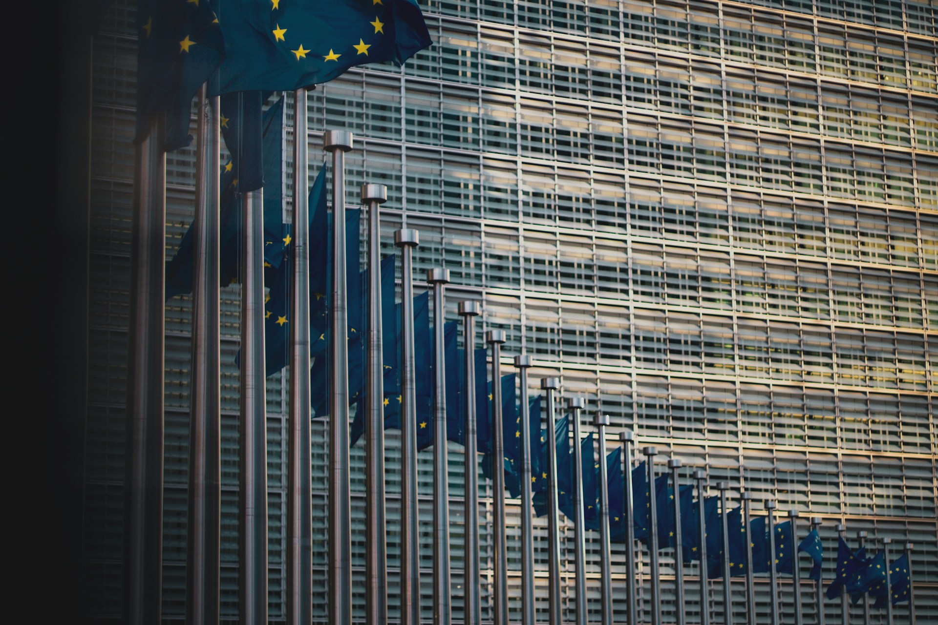 Gebäude mit riesigen Glasfenstern, davor wehen EU-Flaggen, Foto: Unsplash/Christian Lue
