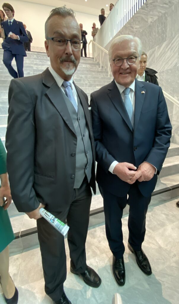 2 Männer in dunklen Anzügen und mit grauem Haar stehen nebeneinander