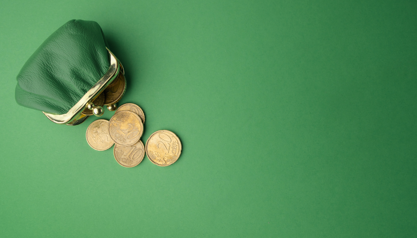 Grüne Geldbörse, aus der ein paar Münzen fallen, auf grünem Hintergrund.