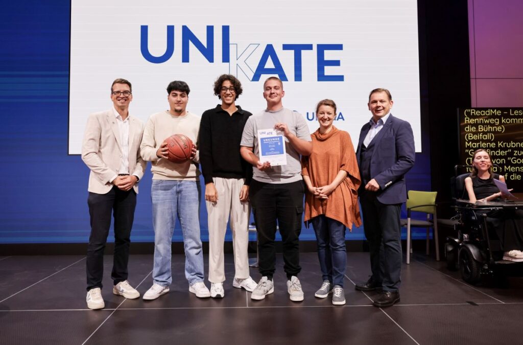 6 Personen stehen auf einer Bühne, ein junger Mann hält einen Basketball, ein anderer eine Urkunde