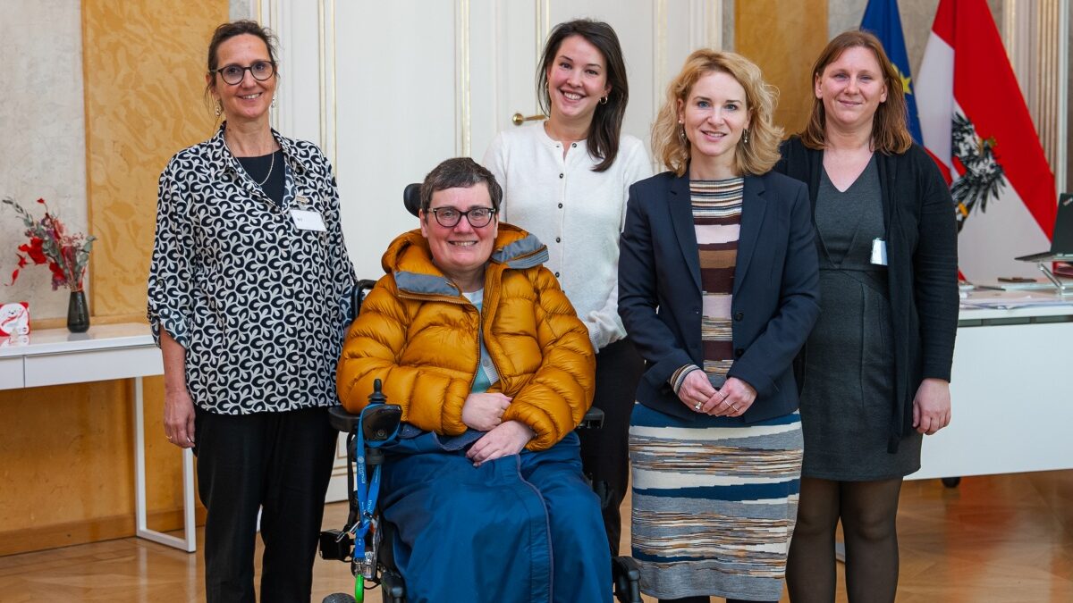 Gruppenfoto von 4 stehenden Frauen und einer in einem Rollstuhl sitzenden Frau, dahinter sind die EU- und die österreichische Fahne zu sehen