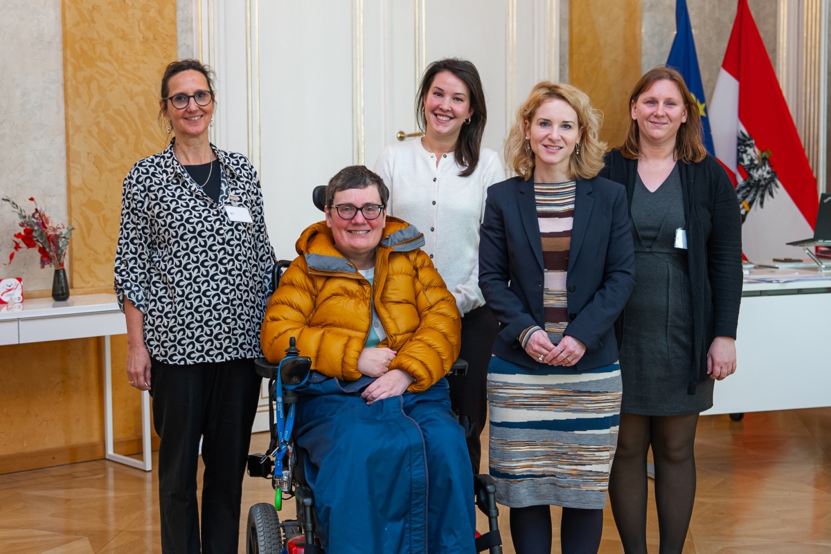 Gruppenfoto von 4 stehenden Frauen und einer in einem Rollstuhl sitzenden Frau, dahinter sind die EU- und die österreichische Fahne zu sehen