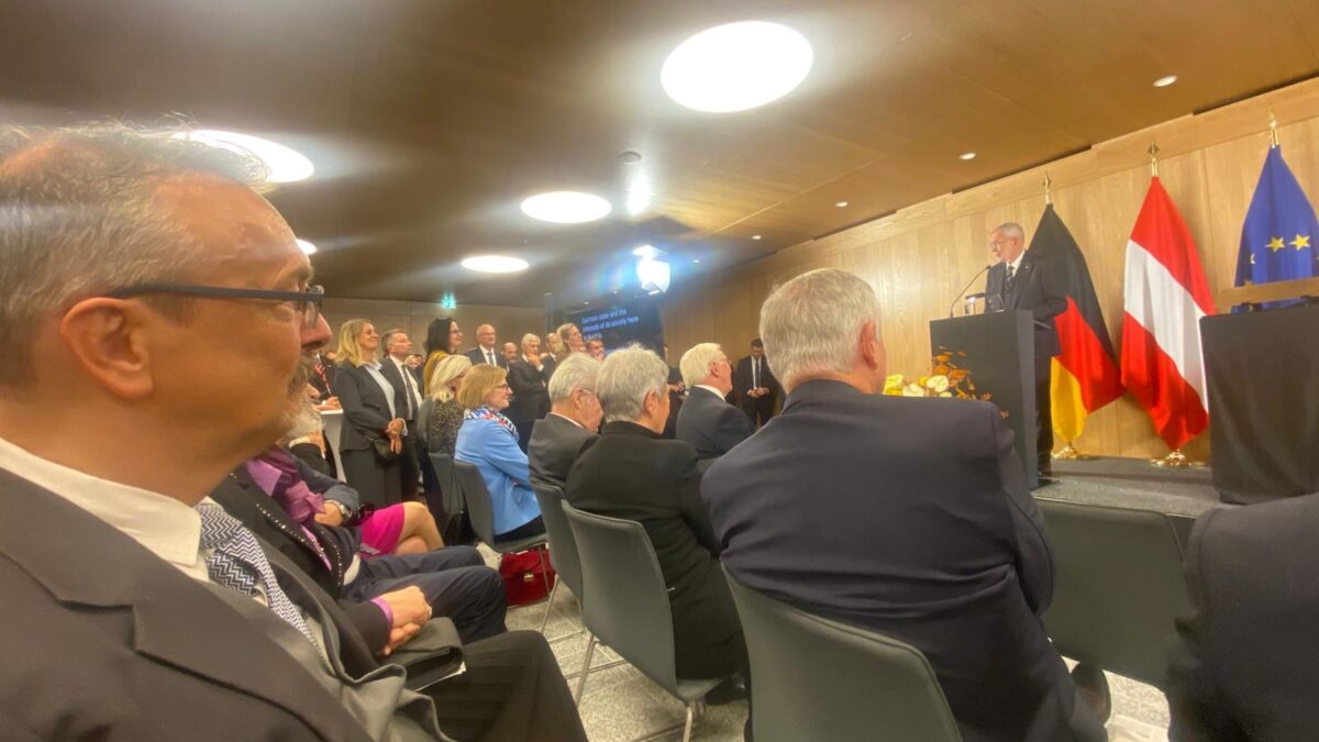 zahlreiche feierlich gekleidete Menschen sitzen auf schwarzen Stühlen