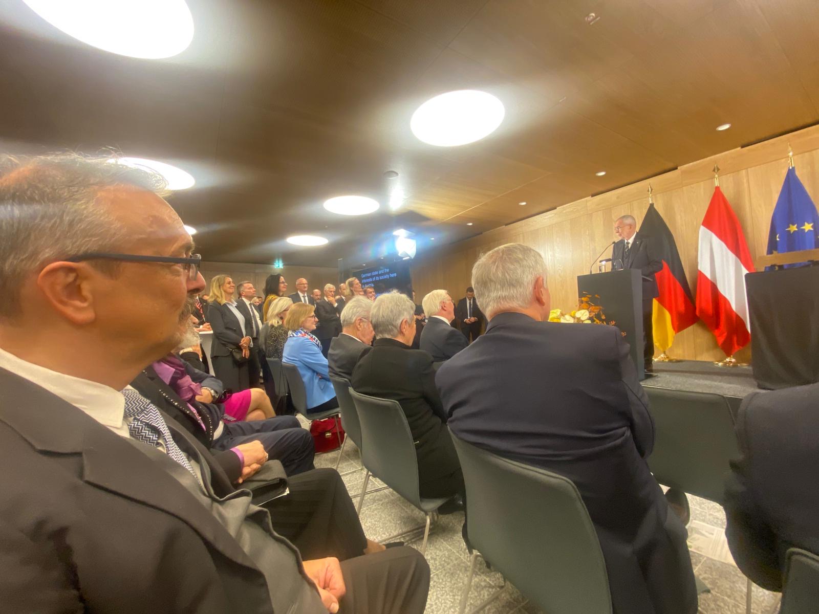 zahlreiche feierlich gekleidete Menschen sitzen auf schwarzen Stühlen