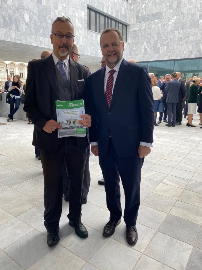 2 Männer in dunklen Anzügen und mit grauem Haar stehen nebeneinander