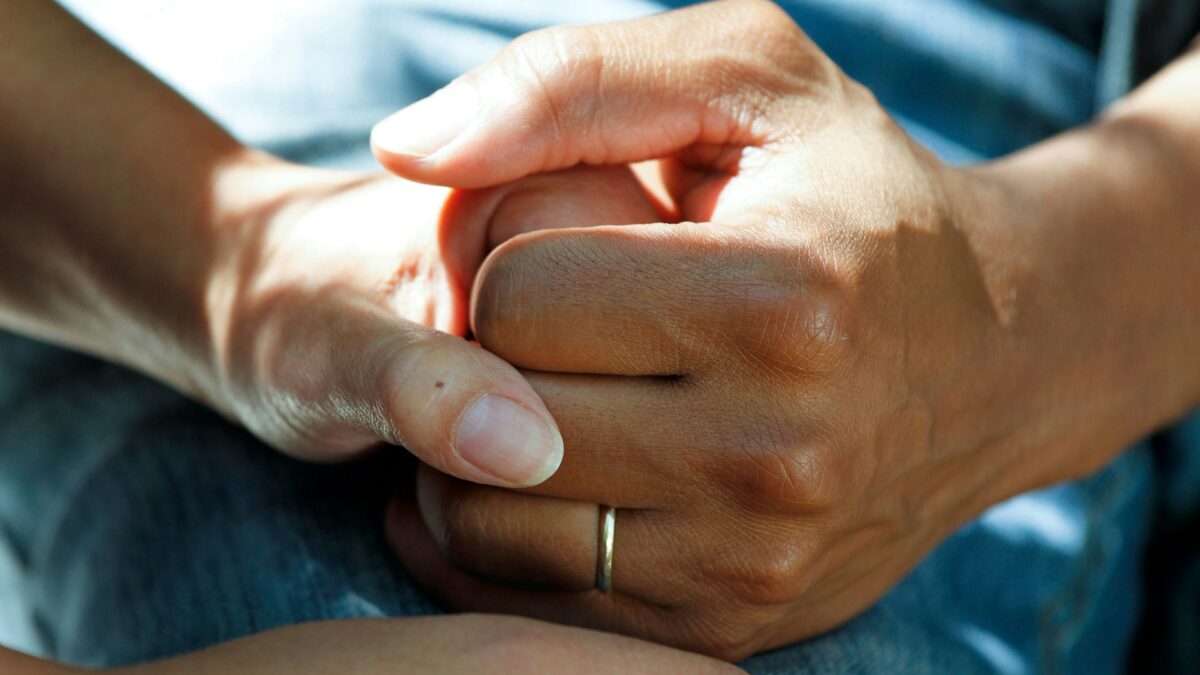 Hand mit goldenem Ehering hält andere Hand auf blauem Hintergrund, Foto: National Cancer Institute