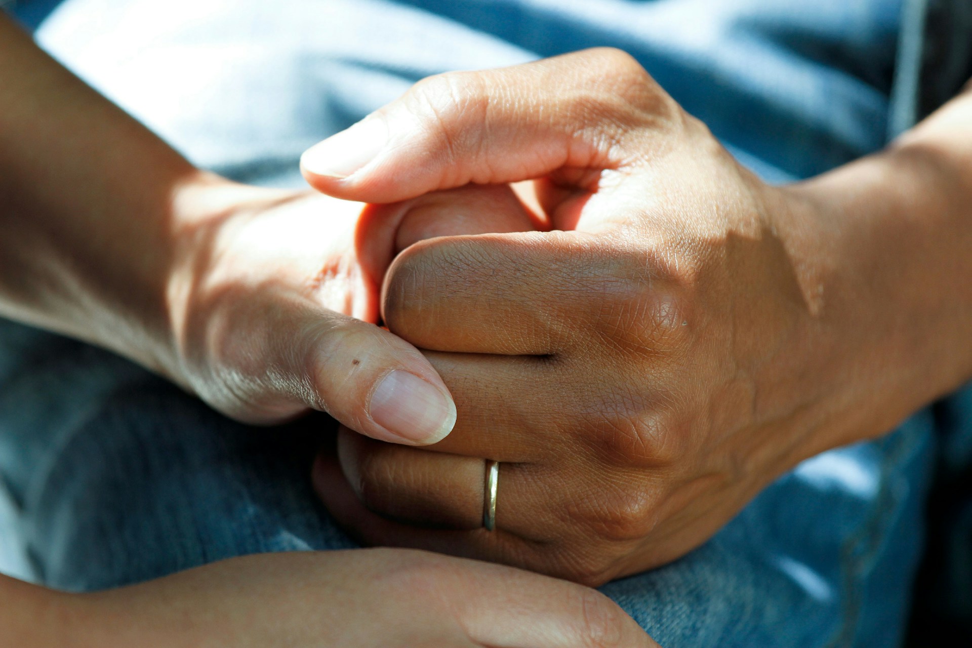 Hand mit goldenem Ehering hält andere Hand auf blauem Hintergrund, Foto: National Cancer Institute