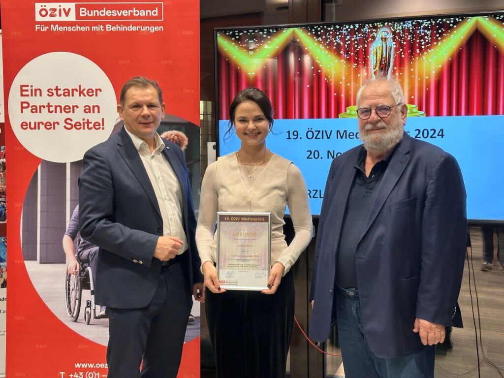 zwei Männer und eine Frau, die eine Urkunde hält, stehen vor einem Rollup