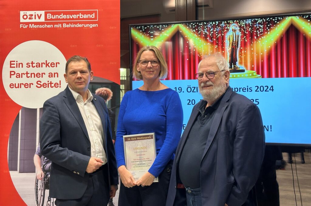 zwei Männer und eine Frau, die eine Urkunde hält, stehen vor einem Rollup