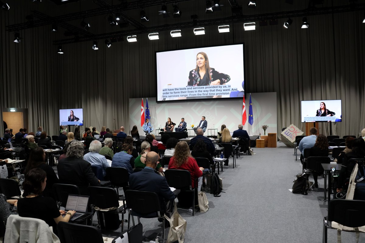 Veranstaltungssaal mit sitzendem Publikum in den Reihen und auf einer Bühne sitzenden Personen