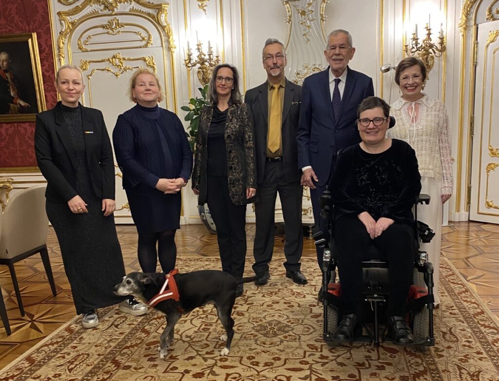 Gruppenbild 5 stehender Personen und einer Frau in einem Rollstuhl im Büro des Bundespräsidenten