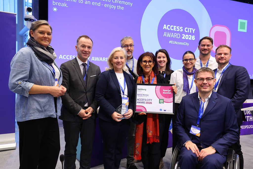 Gruppenbild 10 stehender Personen. Eine Dame in der Mitte hält eine Auszeichnung in Händen.