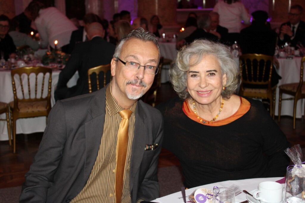 Ein Mann und eine Frau, beide mit grauen Haaren, sitzen nebeneinander in einem Festsaal
