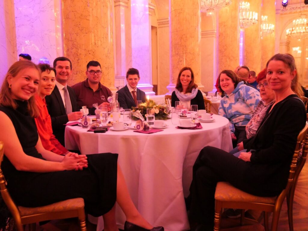 festlich gekleidete Männer und Frauen sitzen rund um einem festlich gedeckten Tisch