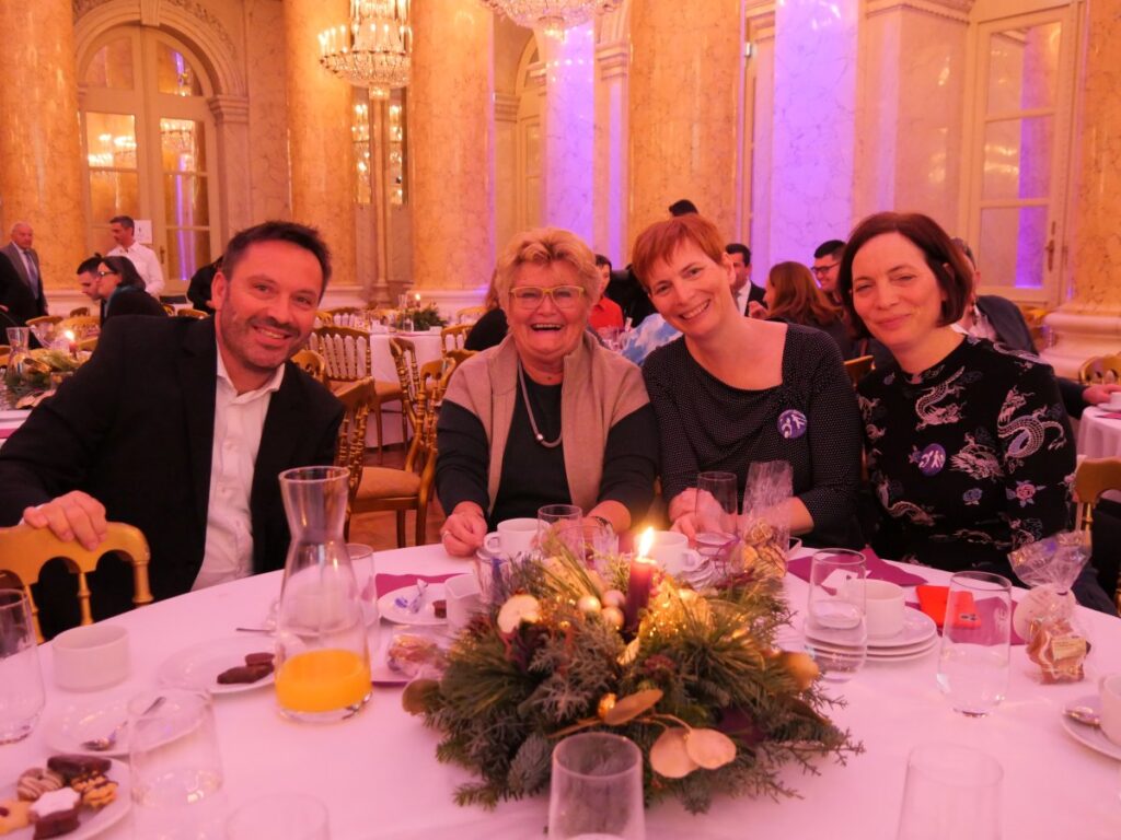 ein Mann und drei Damen, alle festlich gekleidet, sitzen an einem festlich geschmückten Tisch