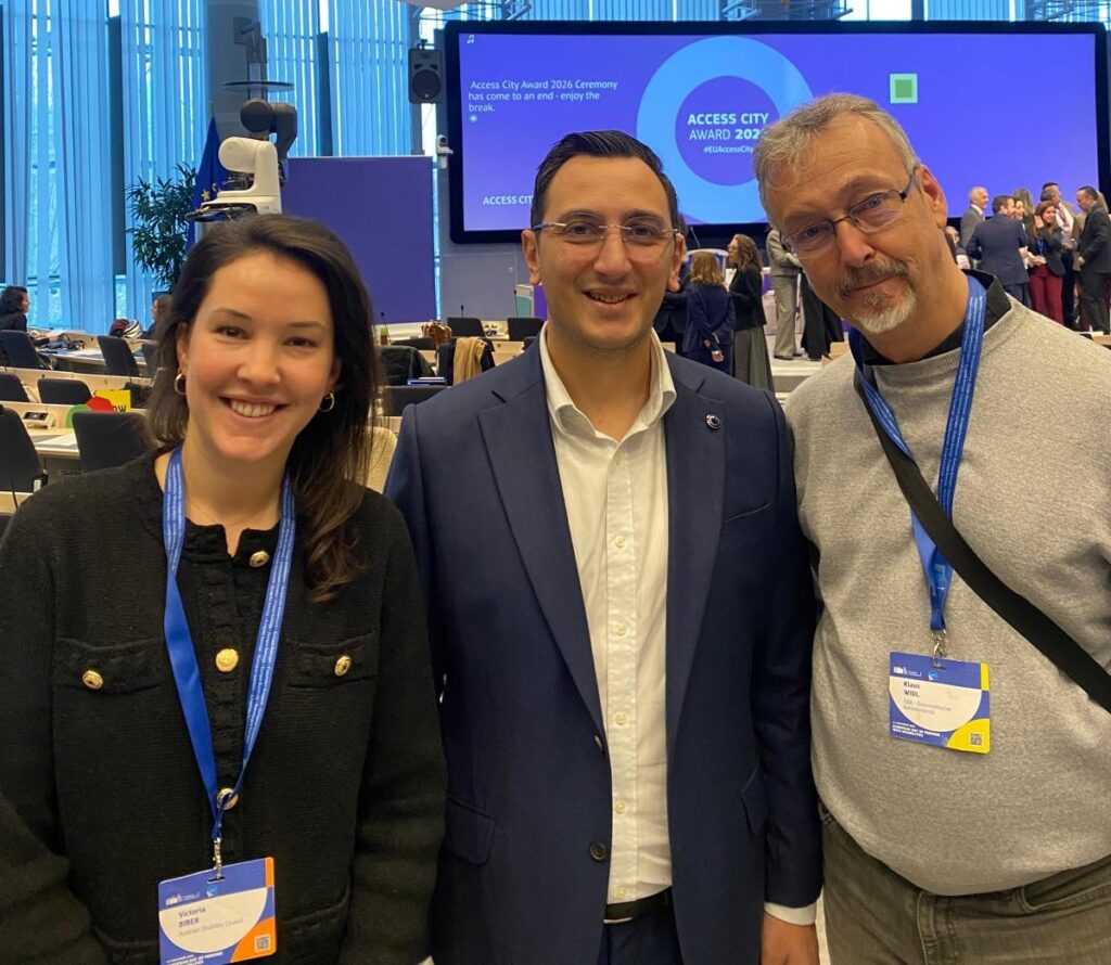 Gruppenbild 3 stehender Personen, eine Frau und zwei Männer, in einem Konferenzsaal