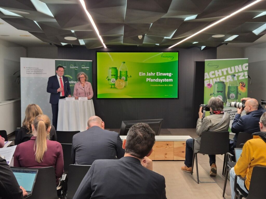 ein Mann und eine Frau stehen vor einem Stehtisch bei einer Pressekonferenz, im Vordergrund Teilnehmer an der Pressekonferenz