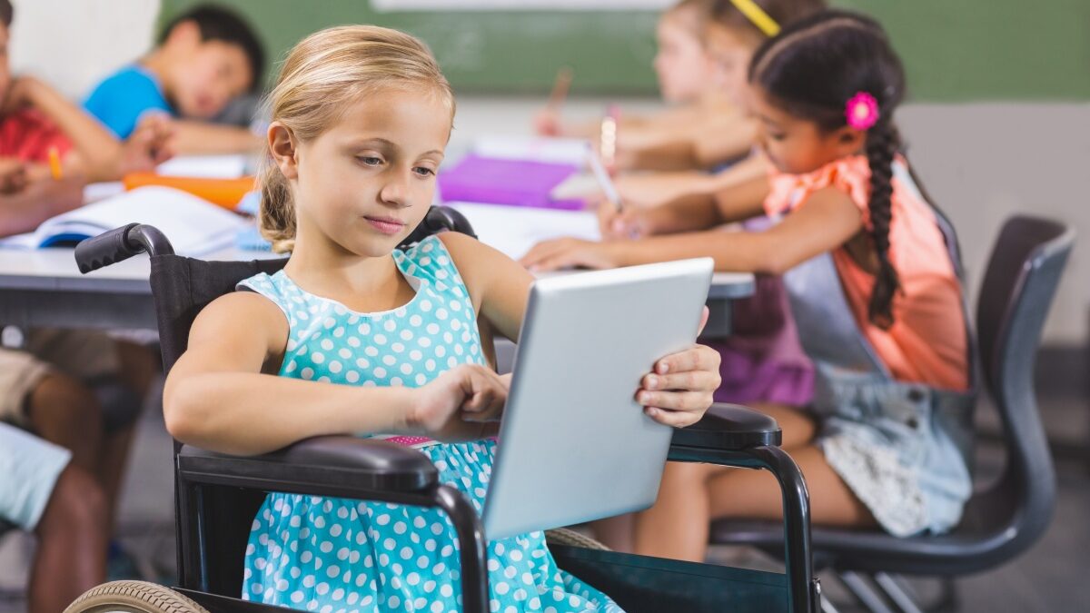 Mädchen im Rollstuhl nutzt ein digitales Tablet und ist in Unterrichtsaktivitäten eingebunden. Andere Kinder sind im Hintergrund beim Lernen zu sehen. Foto: Pikwizard/ Awesome Content
