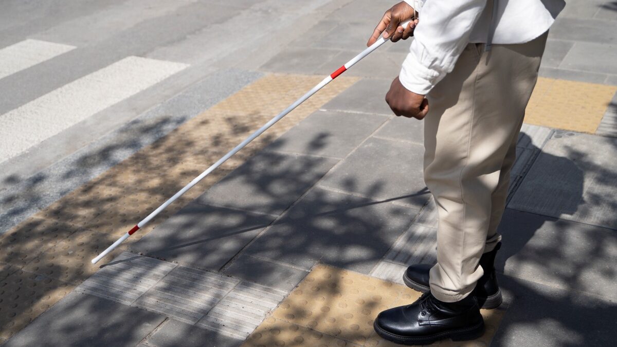 Mann mit Langstock geht über Zebrastreifen, der mit Bodenmarkierungen ausgestattet ist, Foto: freepik.com