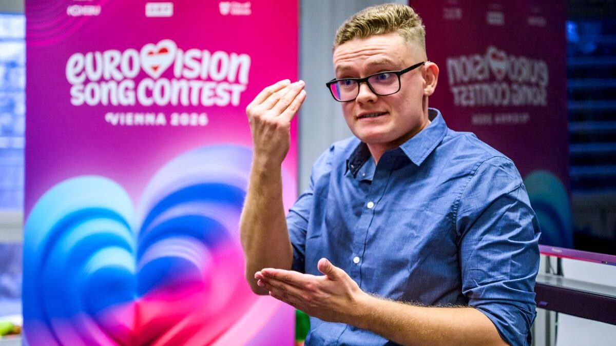 junger Mann mit blauem Hemd und blindem Haar sowie Brille performt in Gebärdensprache