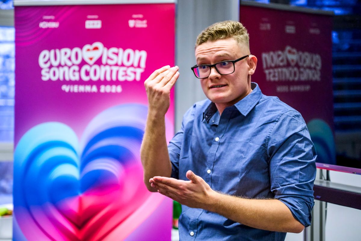 junger Mann mit blauem Hemd und blindem Haar sowie Brille performt in Gebärdensprache