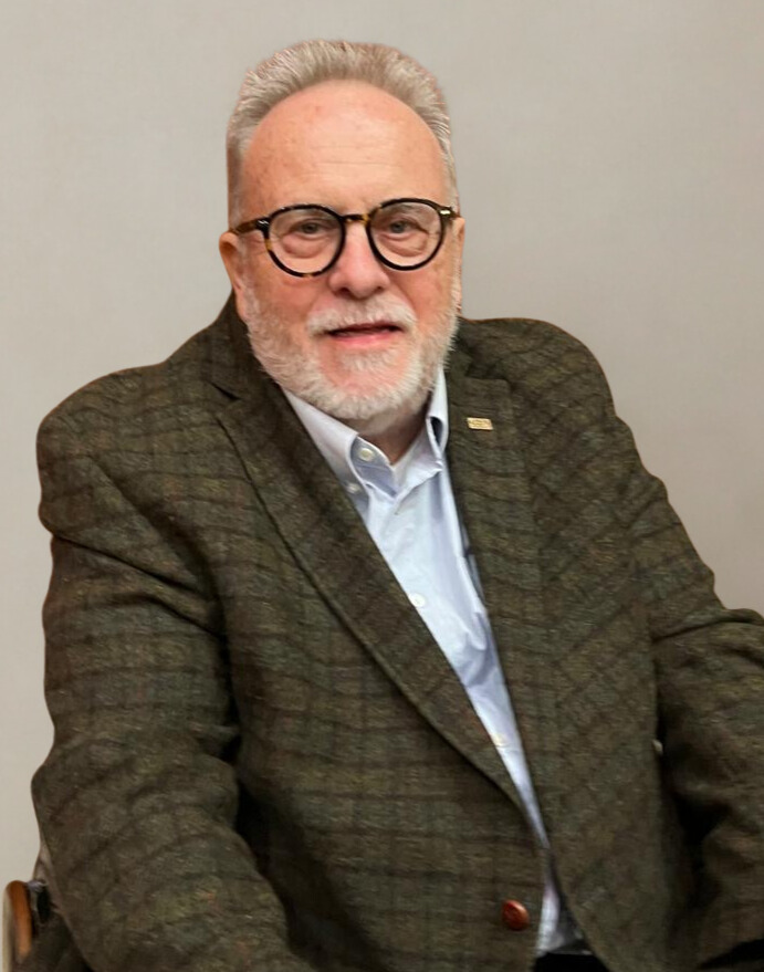 Mann mit grauem Haar, Brille, kariertem Sakko und hellem Hemd sitzt in einem Rollstuhl