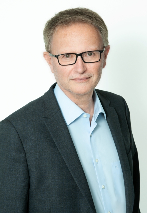 Mann mit brünettem Haar, Brille, blauem Hemd und grauem Sakko