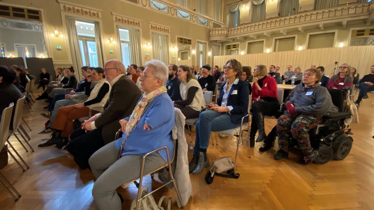 Zahlreiche Menschen sitzen auf Stühlen in einem Festsaal