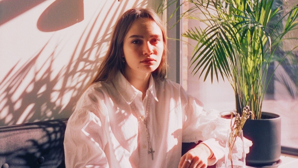 junge Frau sitzt in einem hellen Raum nahe einem Fenster und blickt ruhig nach unten. Foto: Pexels